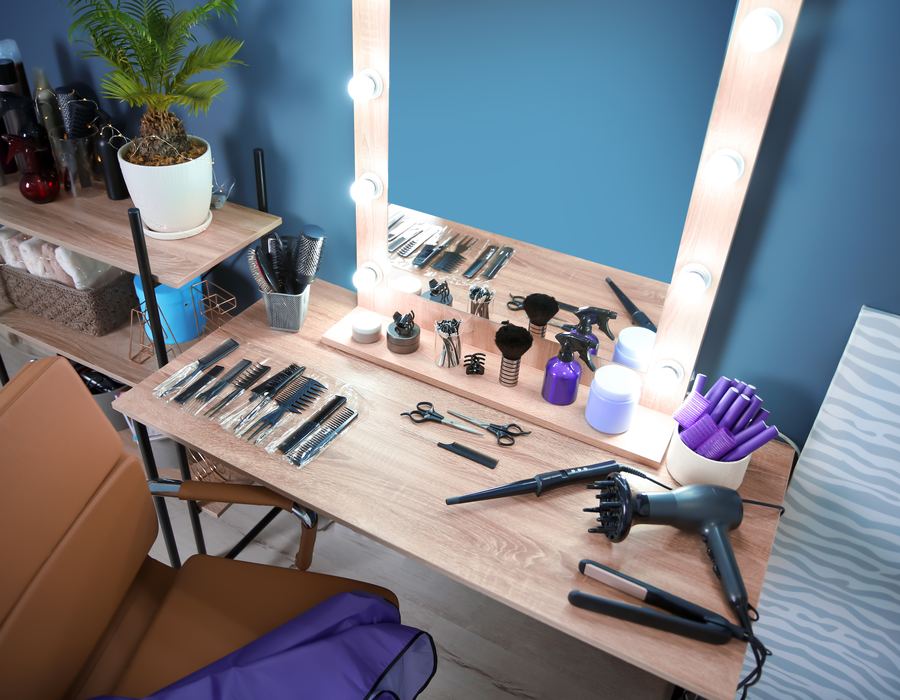 Independent booth renter vanity with Hollywood lights, shears, dryer, and teal wall