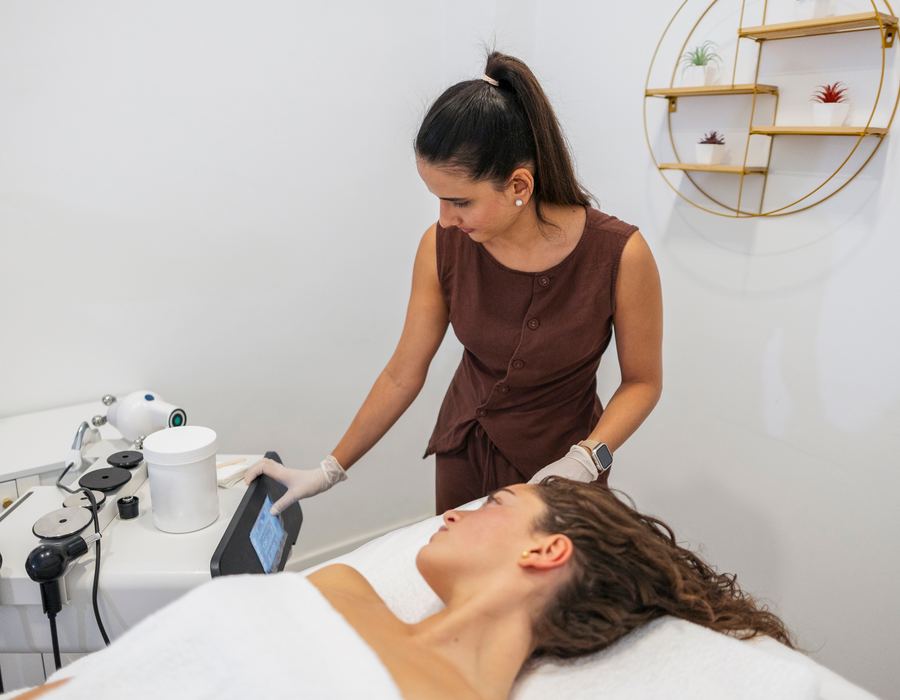 Esthetician in gloves operating a treatment device beside a client on a spa table